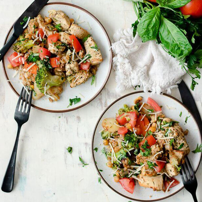 Recipe image of two plates of Italian chicken and farro with cutlery, next to fresh herbs,