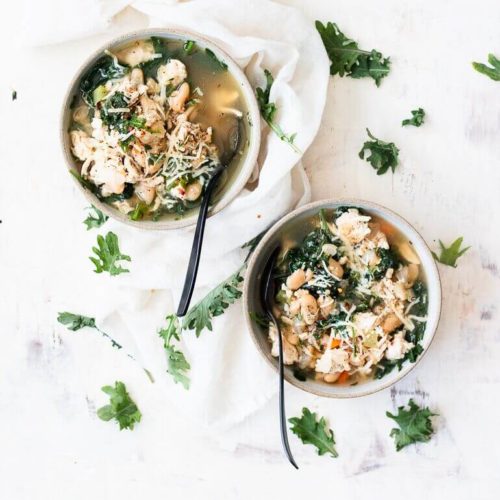 Recipe image of two bowls of weeknight turkey kale soup scattered with baby kale leaves and topped with parmesan cheese
