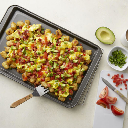 Recipe image of a sheet pan with potatoes, avocado, bacon, cheese, tomatoes and green onions next to raw ingredients